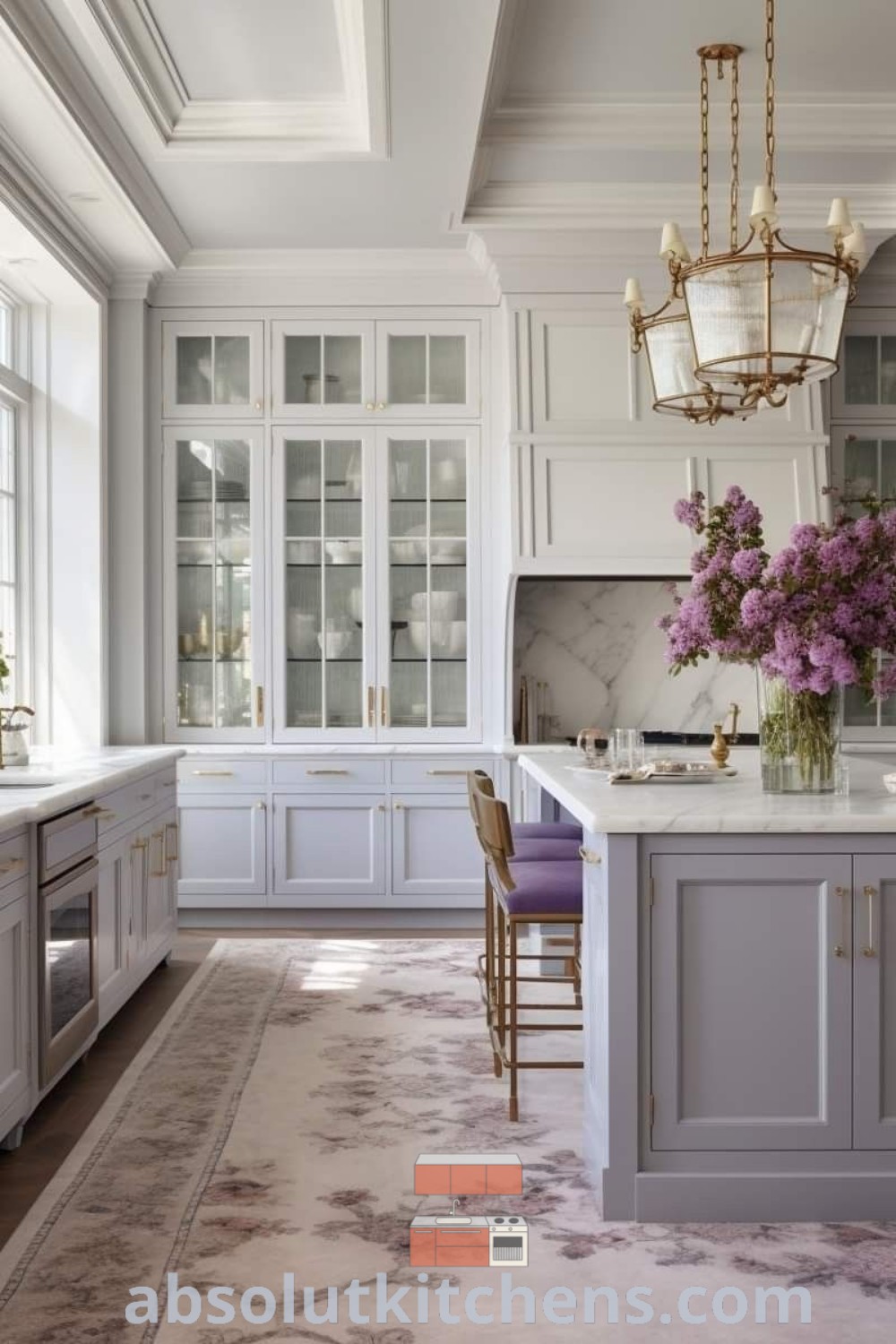 A cozy kitchen with white cabinets adorned with purple flowers in vases, complemented by a chandelier, showcasing classic country kitchen design trends. This inspiring space offers feminine decor ideas and modern classic kitchen aesthetics, found on absolutkitchens.com.