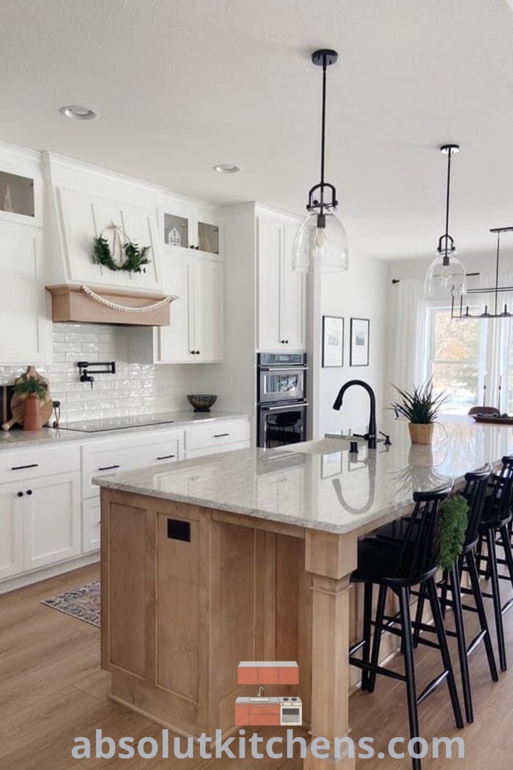 A spacious kitchen showcasing white subway tile accents, elegant white cabinets, and warm wooden flooring. The large island is surrounded by black bar stools, creating a cozy and functional space. This design combines farmhouse elements with modern touches, providing inspiring decor ideas for new house kitchens. Visit absolutkitchens.com for more decor inspirations.