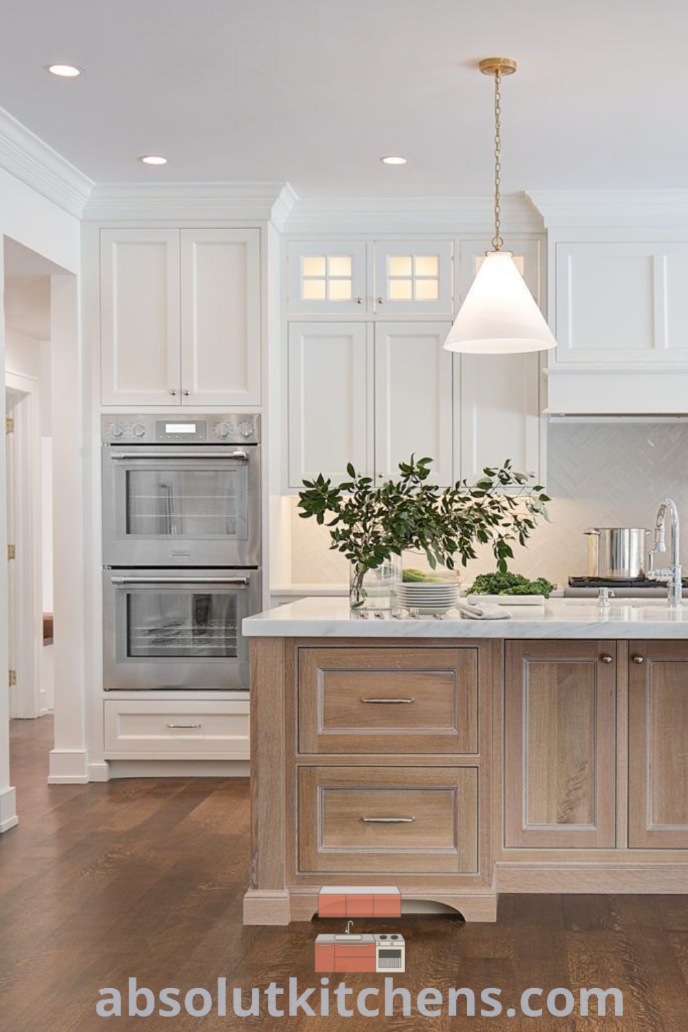 A large coastal kitchen with white cabinets, wood flooring, and an island topped with a potted plant, showcasing inspiring decor ideas for house or apartment designs. Find timeless kitchen inspirations and ideas you need to see at absolutkitchens.com.