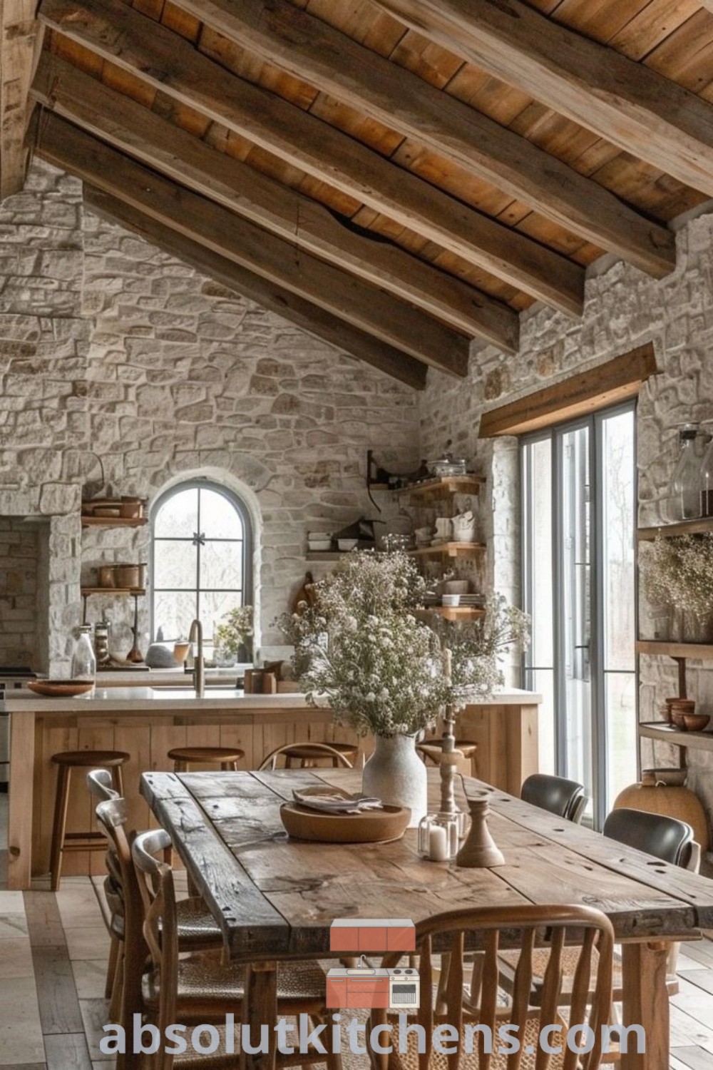 A rustic dining room with stone walls and exposed beams, featuring a wooden table surrounded by chairs. This space exemplifies farmhouse trends and cozy aesthetic, offering design tips and inspiring decor ideas for the perfect kitchen and dining room. Find more unique inspirations at absolutkitchens.com.