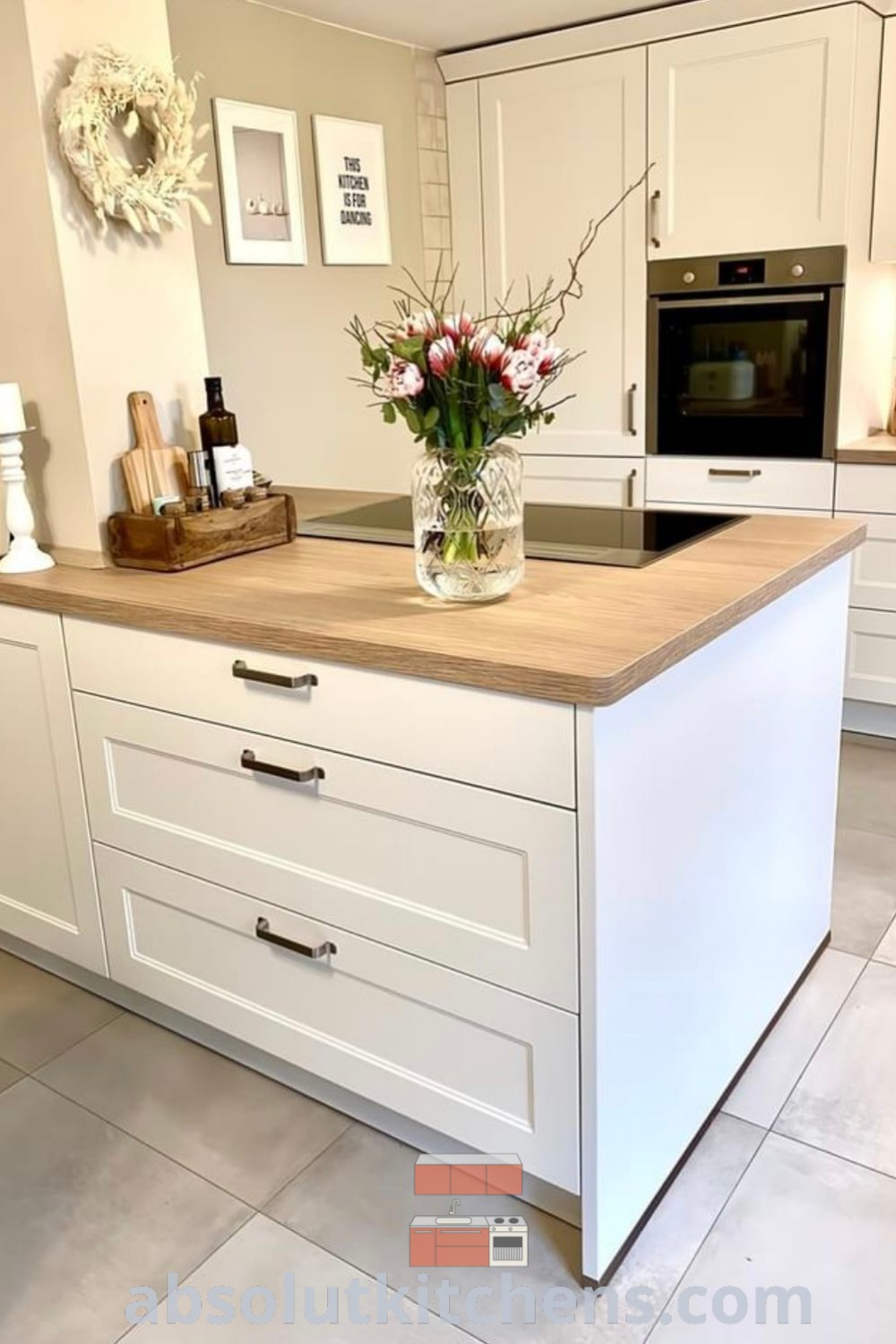 A stylish open plan kitchen with a vase of flowers on the island, showcasing a modern white kitchen design. This kitchen decor blends aesthetics and functionality, featuring creative kitchen backsplash designs. Explore more cozy home decor ideas and inspirations at wellnesswink.com.