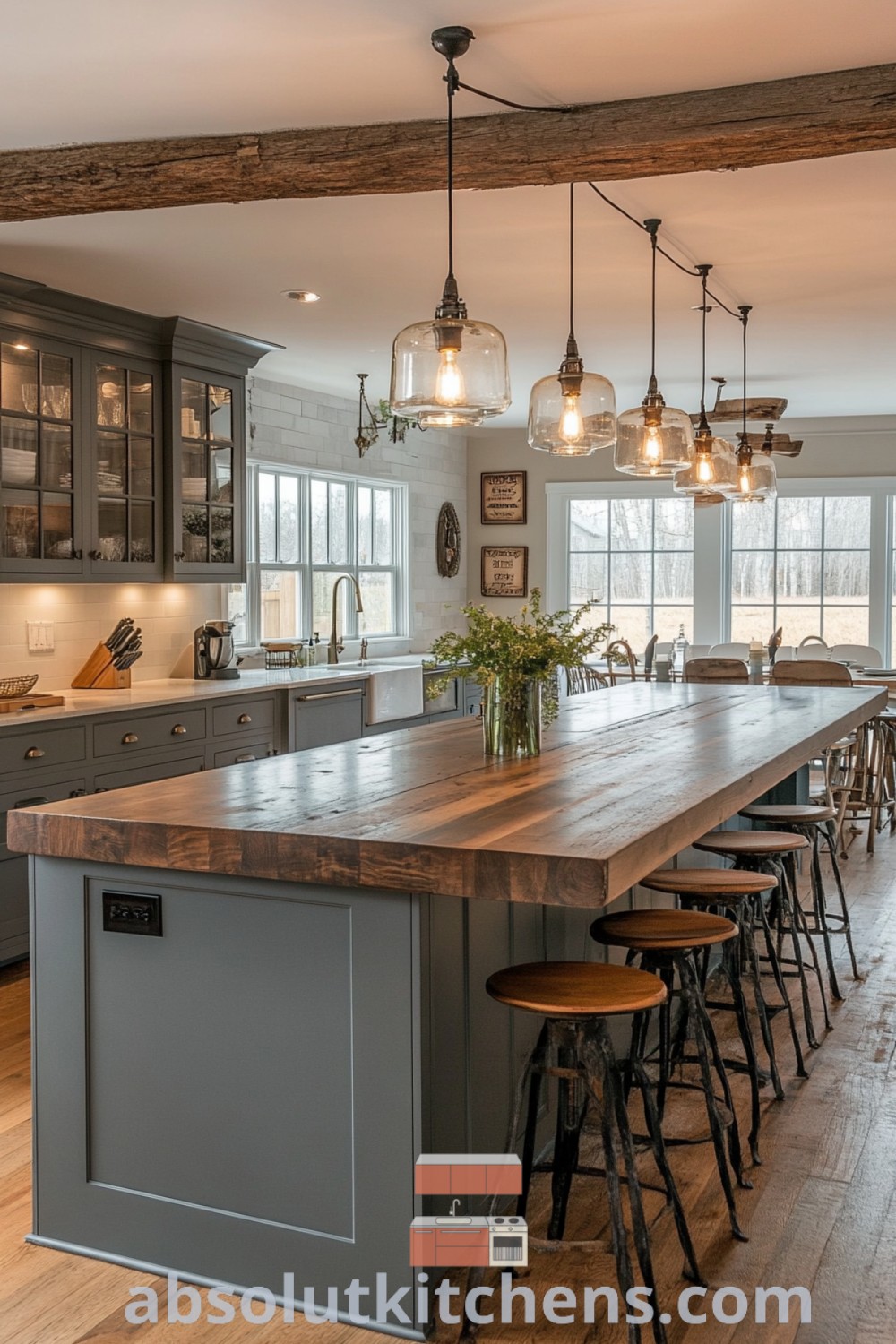 A large kitchen island with stools, illuminated by hanging lights, exemplifies modern farmhouse style. This dynamic kitchen showcases silver fixtures and blends rustic elements with a cozy aesthetic, offering design ideas for modern homes. Explore more design tips at absolutkitchens.com.