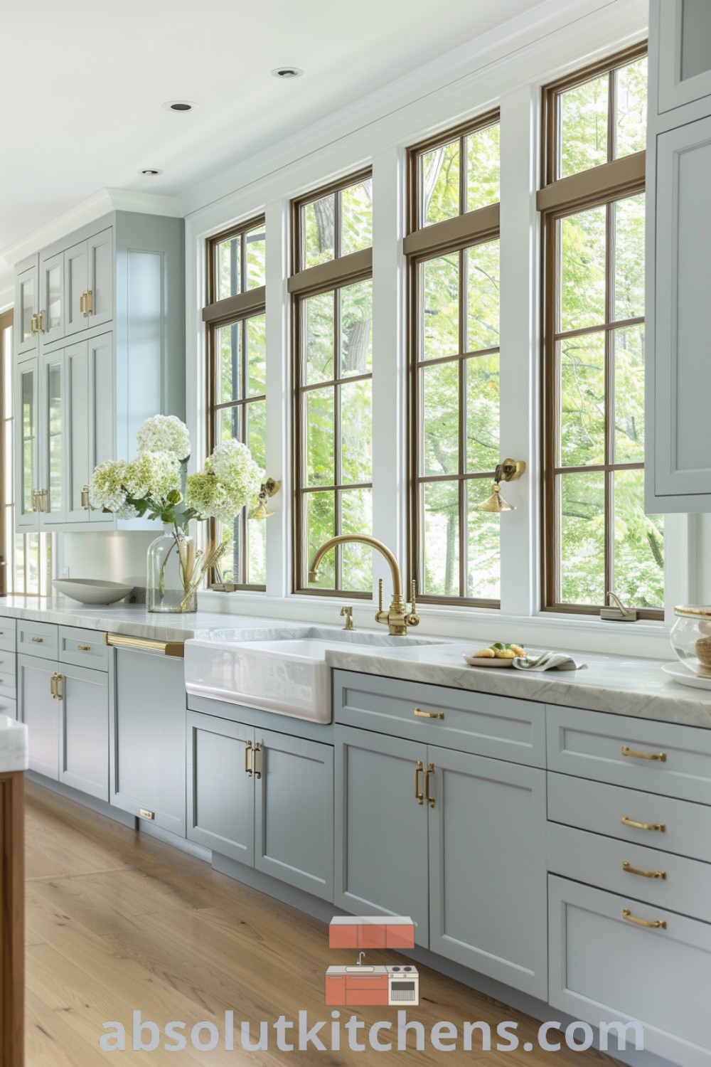 A large French Mediterranean kitchen with white cabinets, gold trim on the windows, and wooden flooring, offering design ideas you need to see for your house or apartment. This inspiring space blends French inspired interior design with cozy aesthetics, showcasing unique kitchen decor ideas for a welcoming atmosphere at absolutkitchens.com.